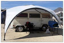Setting up camp at Burning Man. My old Volkswagen fit perfectly under this 15' Coleman canopy. I positioned everything so I would have morning shade, so I could sleep in a little before it got too hot. I kept a water jug, an extra chair, and some gear on top of my camp chair. The small blue tarp stayed put nicely after I tucked it under the milk crates covering my dry food and cooking gear. Keeping things tidy kept people from prying and esepecially helped to keep the wind from carrying things away.